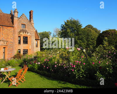 Chenies Manor House an einem spätsommerabend vor blauem Himmel mit Cosmos, Dahlien und Cleome mit schleichender Schatten auf dem Rasen. Stockfoto