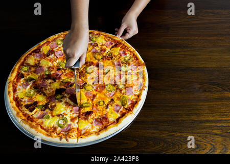 Hand schneiden eine hausgemachte Pizza mit pizza Cutter auf Tisch. Stockfoto