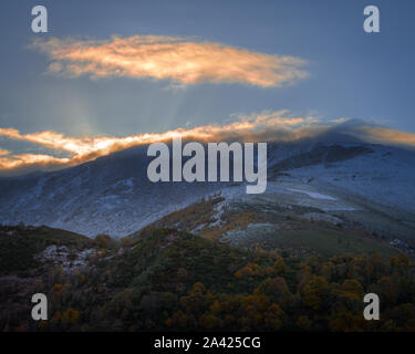 Strahlen der aufgehenden Sonne durch die Wolken, die die Berge Krone in einem Tag der Anfang Herbst in der ancares Bergkette Stockfoto