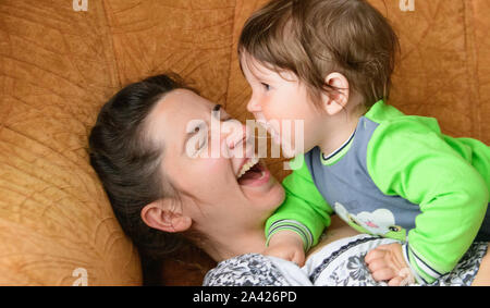 Baby beißt Mammen Nase. Glückliche Mutter mit Baby. Ein Junge beißt sich Mütter Nase auf der Couch. Spaß mit Ihrer geliebten Mutter Stockfoto