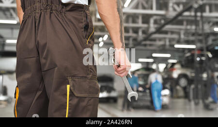 Ansicht von der Rückseite der Handwerker in Overall in Werkstatt und Schraubenschlüssel in der Hand zu halten. Auto Techniker arbeiten in Auto Service und Reparatur von Automobilen. Konzept der Pflege und Auto zur Festsetzung. Stockfoto