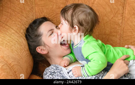 Baby beißt Mammen Nase. Glückliche Mutter mit Baby. Ein Junge beißt sich Mütter Nase auf der Couch. Spaß mit Ihrer geliebten Mutter Stockfoto