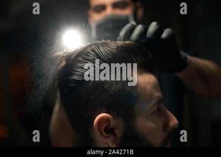 Der dunkelhaarige Mann s Kopf mit sauber nasse Haar, das von männlichen Friseur Kämmen in schwarz Handschuhe. männlichen jungen Bartgeier im barbershop seinem Haarschnitt Mehr trendige und stilvolle ändern Stockfoto