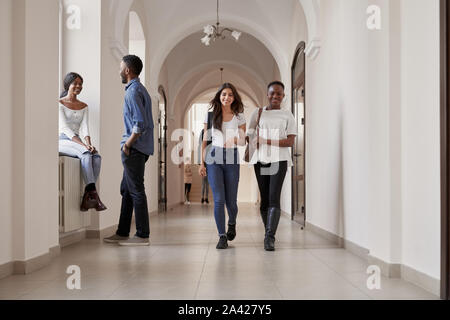 Multirassischen schöne glückliche Schüler, leger gekleidet, Wandern in der Universität Halle und sitzen auf fensterbank während der Pause zwischen den Vorlesungen. Sind eine Gruppe von Jugendlichen, die Rest zusammen Stockfoto