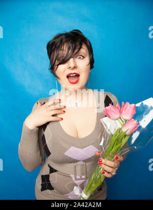 Schöne Mädchen in die niedliche Pullover mit Blumen Tulpen in den Händen auf einem blauen Hintergrund allein Stockfoto