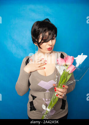 Schöne Mädchen in die niedliche Pullover mit Blumen Tulpen in den Händen auf einem blauen Hintergrund allein Stockfoto