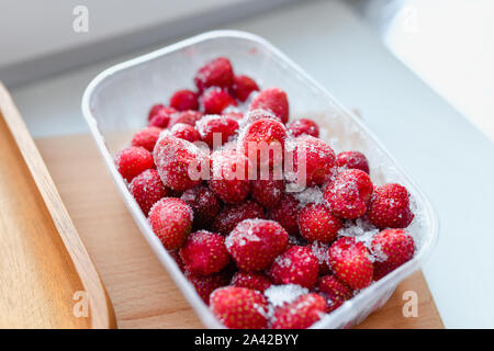 Gefrorene Erdbeeren in Kunststoff. Gefrorene Erdbeeren in einem Kunststoffbehälter im Gefrierfach. Gefrorene Beeren Stockfoto