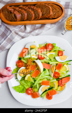 Senf Gemüse Salat geben. Gemüsesalat mit menschlichen Händen. auf einem weißen Teller. Gewürze hinzufügen. Stockfoto