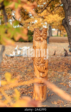 Holz- owl Totem in einem forest park. Die Bäume sind wahrscheinlich sichtbar des gleichen Typs, aus dem die Statuen geschnitzt werden. Schnitzereien aus Holz Idol in einem Stockfoto