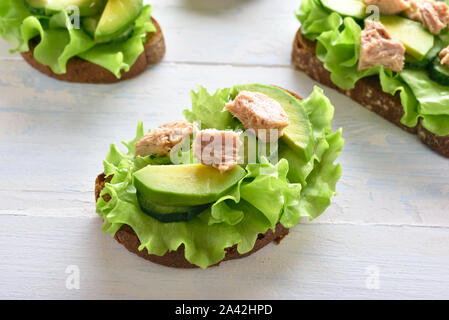 In der Nähe von Thun Sandwiches mit Avocado und Salatblätter auf hellem Holztisch. Lecker Thunfisch Brötchen zum Frühstück. Gesunden Snack. Stockfoto