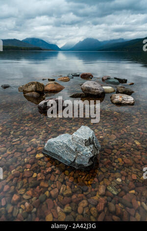 Eine Reihe von Felsformationen auf See Macdonald mit der Aussicht auf die Berge im Hintergrund und klares Wasser an einem bewölkten Tag, Montana. Stockfoto