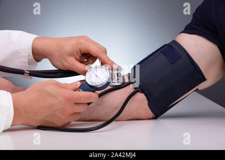 In der Nähe von Doktor Kontrolle Blutdruck Der männlichen Patienten auf dem Tisch gegen grauer Hintergrund Stockfoto