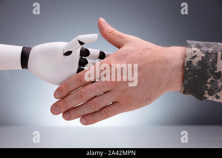 In der Nähe von militärischen Mann die Hände schütteln mit Roboter gegen grauer Hintergrund Stockfoto