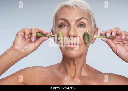 Schöne Dame mittleren Alters rolling Jade Walzen auf ihren Wangen Stockfoto