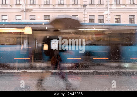 Abstrakte Silhouette des Menschen unter dem Dach, mit dem Bus, Stadt, Straße durch Regentropfen auf dem Fenster Glas gesehen, verschwommene Bewegung. Jahreszeiten, Wetter, Stadt Stockfoto