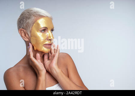 Schön gealterte Frau zur Seite schauen beim demonstrieren ihr Gold Maske Stockfoto
