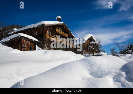 Zwei Holz- Ski Chalets und eine kleine Scheune von und mit Schnee bedeckt unter einem blauen Himmel im Winter in einem Skigebiet in Tirol, Österreich umgeben. Stockfoto