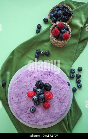 Eis Käsekuchen und Beeren auf einem Hintergrund in grün Tönen. Mit einem Korb von Blaubeeren, Brombeeren und Himbeeren begleitet. Stockfoto