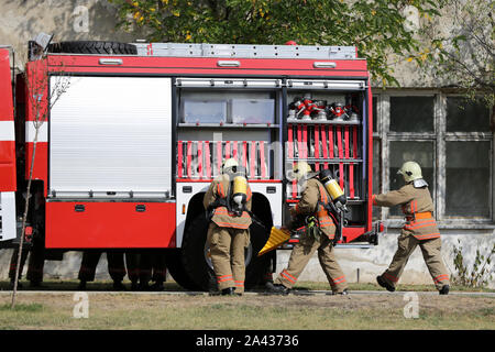 Feuerwehrmänner, die Teilnahme an einer Schulung, wo sie Feuer aus einem Auto Löschen in einem anderen Fahrzeug zusammengestoßen. Red fire truck, Fire Engine. Stockfoto