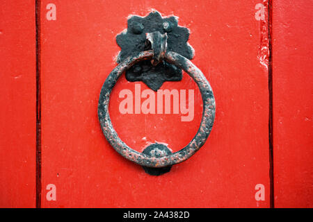 Bügeleisen antik Ring auf rotem Holz- Türgriff. Close-up, ein Fragment der Tür, frontalen Aufnahmen Stockfoto