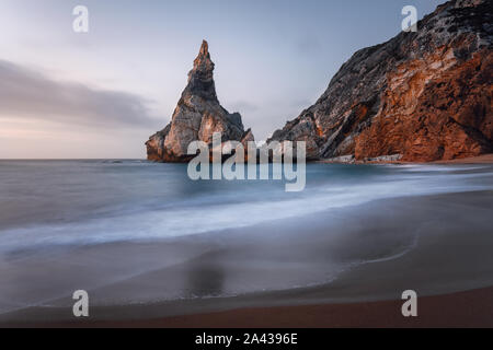 Ursa Strand im Sonnenuntergang Abendlicht. Sintra, Portugal. Surreale Sandstrand mit riesigen hoch aufragenden Felsen und sanften Wellen am Atlantik Küste Landschaft Stockfoto