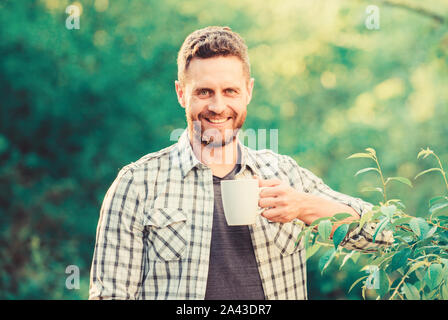 Erfrischendes Getränk. Man bärtige Kaffee Bauer halten Becher Natur Hintergrund. Grüner Tee Plantage. Vollständige blatt Tee. Hervorragender Geschmack. Genießen Sie heiße Getränke. Natürliche trinken. Gesunde Lebensweise. Ich bevorzuge grünen Tee. Stockfoto