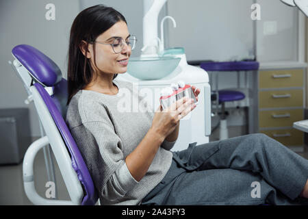 Junge weibliche Patienten sitzen auf Stuhl in der Zahnarztpraxis. Vorbereitung für die Zahnärztliche Prüfung. Mit Blick auf die Kamera Stockfoto