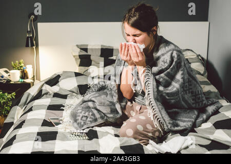 Kranke Frau mit laufender Nase, im Bett sitzen. Frau Unwohlsein und niesen Schlafzimmer. Frau mit Gewebe, grippeartige Symptome. Healthcare Medical Konzept Stockfoto