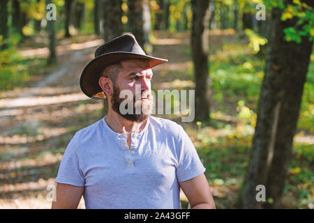 Cowboy Stil. Mann hipster im Herbst Wald entspannen. Frühling sonniges Wetter. Camping und Wandern. reife Männer mit brutaler aussehen. Bärtiger Mann in cowboyhut Spaziergang im Park Outdoor. Schwere brutale Hipster. Stockfoto