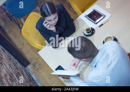 Zwei junge männliche und weibliche multirassischen Geschäftsleute arbeiten mit technischen Geräten an der Bar angeschlossen. Zwei junge kreative Mitarbeiter arbeiten wi Stockfoto