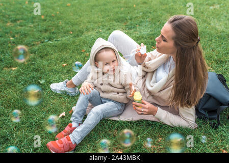 Kleinen Jungen 3-5 Jahre alter Sohn, Fänge Luft- und Seifenblasen. Mom Frau spielt und bläst Seifenblasen, gerne spielen, Spaß haben, im Herbst auf grünem Gras in Stockfoto