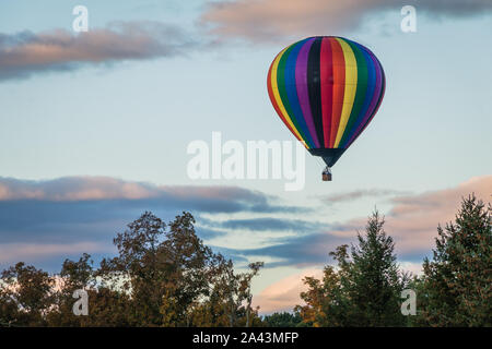 Rainbow Heißluftballon schwebt über auf dem Feld bei Sonnenaufgang Stockfoto