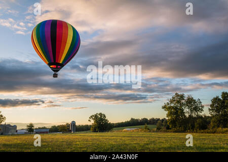 Rainbow Heißluftballon schwebt über auf dem Feld bei Sonnenaufgang Stockfoto