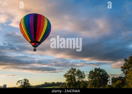 Rainbow Heißluftballon schwebt über auf dem Feld bei Sonnenaufgang Stockfoto