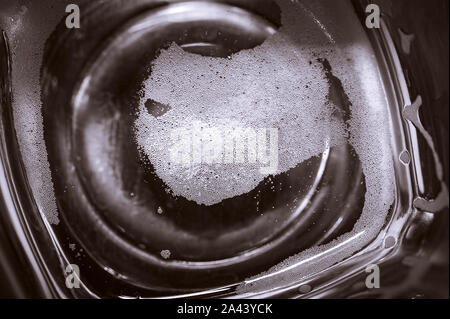 Top-down-Sicht auf Platz unten Leer Bier Glas auf dunklen Tischfläche. Blasen Links aus dem Bier Kopf oder Kragen, cremiger Schaum auf dem Glas. Stockfoto