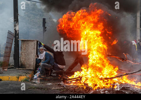 Quito, Ecuador. 11 Okt, 2019. Die Teilnehmer an einer Demonstration sitzen neben einer brennenden Barrikade. Am Freitag, gab es schwere Auseinandersetzungen mit der Polizei in neue Protestaktionen gegen die Erhöhung der Treibstoffpreise in Ecuador. Credit: Sara Bandes/dpa/Alamy leben Nachrichten Stockfoto