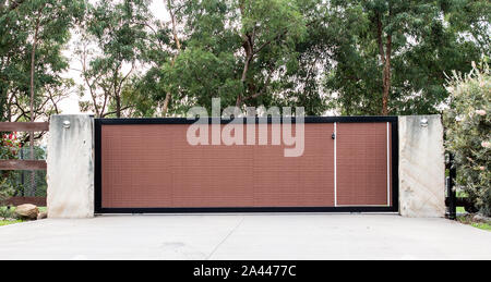 Schwarz Braun metall Schmiedeeisen Auffahrt Eigenschaft Eingangstore in Beton Ziegel Zaun, garten Bäume im Hintergrund Stockfoto