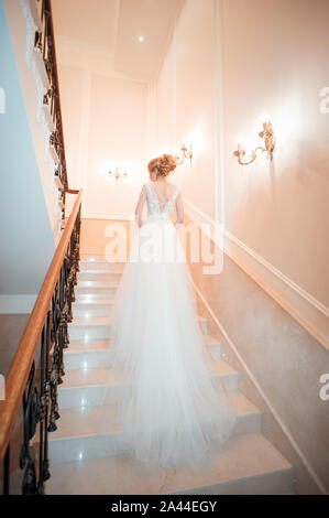 Ein Mädchen in einem Kleid klettert die Treppe hoch. Schöne Dame in einem luxuriösen Ballkleid die Treppen. Kunst Elemente Geländer auf beiden Seiten. Vintage Konzept Stockfoto