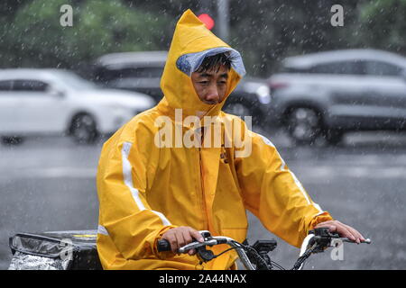 Ein Radfahrer tragen einen Regenmantel und einen Hut gegen schwere Unwetter von Typhoon typhoon Wipha, die 7. des Jahres verursacht, fährt auf einer Straße in der Stadt Guangzhou Stockfoto