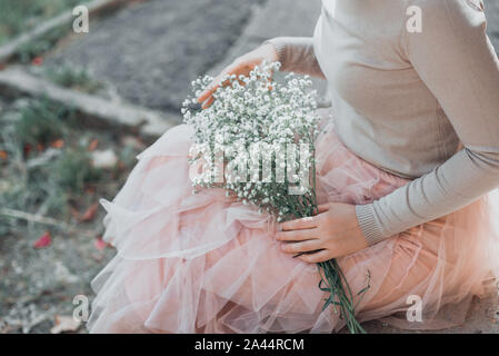 Frau in rosa spitze Rock mit weißen Blumen in den Händen Blumenstrauß sitzt auf der Treppe. Stockfoto