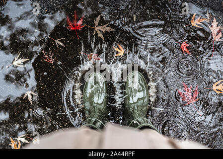 Füße in Olivgrün Gummistiefel in einer Pfütze mit Laub und spritzt. Stockfoto