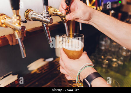 Nahaufnahme eines männlichen Barkeeper abfüllen Bier in einem Pub mit einem großen Glas Krug unter einem Zapfen Anlage auf einem Edelstahl Fass Stockfoto