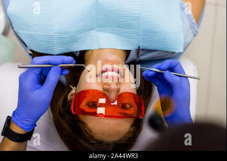 Lächelnde Frau in orange Schutzbrille lehnte sich auf Stuhl in der zahnmedizinischen Zimmer Stockfoto