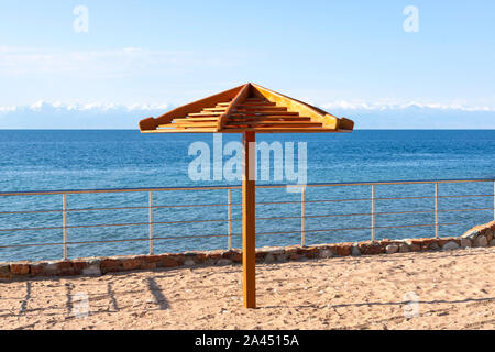 Sonnenschirm close-up am Strand des Sees Issyk-Kul mit schneebedeckten Bergen am Horizont. Kirgisistan Stockfoto