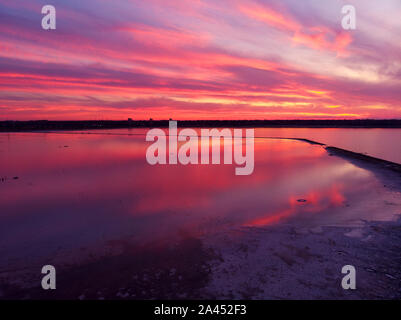 Luftaufnahme von Drone geschossen über der Wasseroberfläche in der Dämmerung, goldenen Stunde Sonnenuntergang. Fantastische Aussicht, Firth reflektierende Oberfläche majestätischen roten und rosa Wolken. Stockfoto