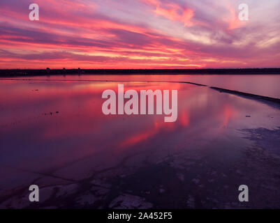 Luftaufnahme von Drone geschossen über der Wasseroberfläche in der Dämmerung, goldenen Stunde Sonnenuntergang. Fantastische Aussicht, Firth reflektierende Oberfläche majestätischen roten und rosa Wolken. Stockfoto