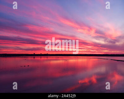 Luftaufnahme von Drone geschossen über der Wasseroberfläche in der Dämmerung, goldenen Stunde Sonnenuntergang. Fantastische Aussicht, Firth reflektierende Oberfläche majestätischen roten und rosa Wolken. Stockfoto