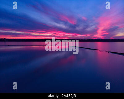 Luftaufnahme von Drone geschossen über der Wasseroberfläche in der Dämmerung, goldenen Stunde Sonnenuntergang. Fantastische Aussicht, Firth reflektierende Oberfläche majestätischen roten und rosa Wolken. Stockfoto