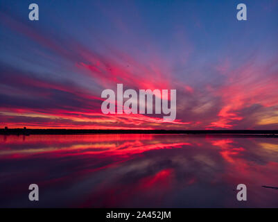 Luftaufnahme von Drone geschossen über der Wasseroberfläche in der Dämmerung, goldenen Stunde Sonnenuntergang. Fantastische Aussicht, Firth reflektierende Oberfläche majestätischen roten und rosa Wolken. Stockfoto