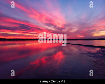 Luftaufnahme von Drone geschossen über der Wasseroberfläche in der Dämmerung, goldenen Stunde Sonnenuntergang. Fantastische Aussicht, Firth reflektierende Oberfläche majestätischen roten und rosa Wolken. Stockfoto